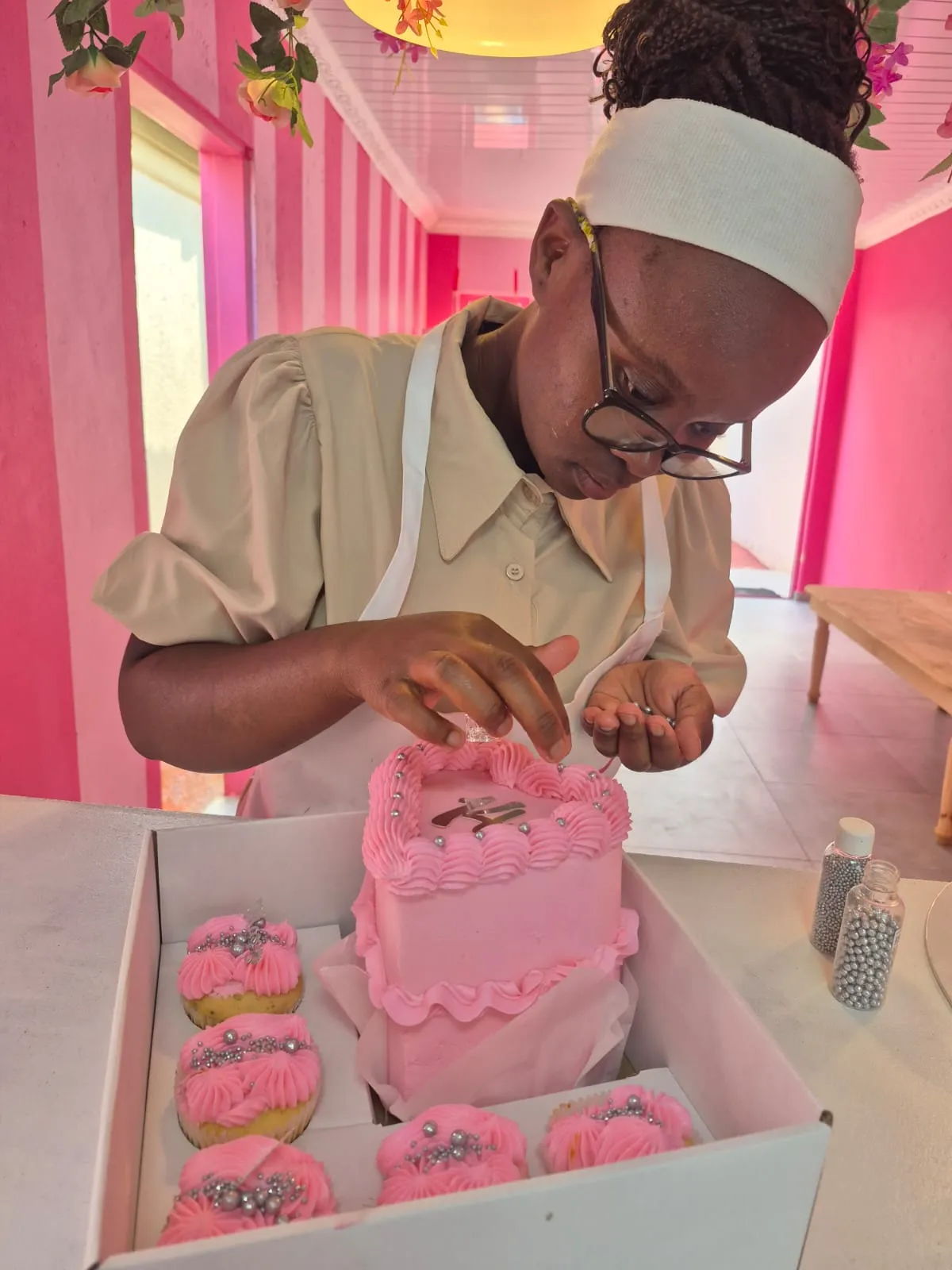 A Rosy's Cakes and Events trainee decorating a pink celebration cake with sugar pearls