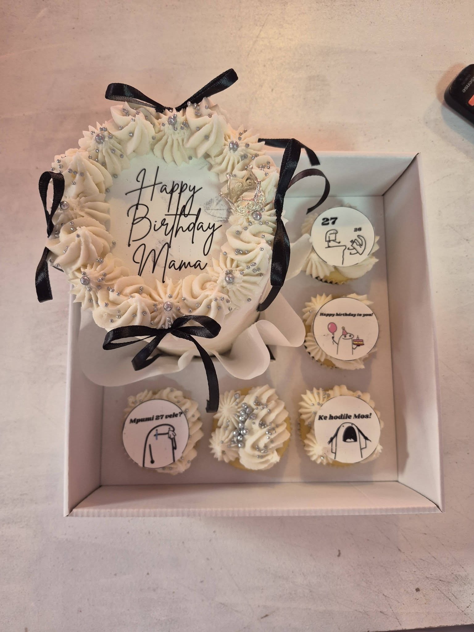 A white birthday cake with black satin ribbons and rhinestone details, made by Rosy's Cakes and Events